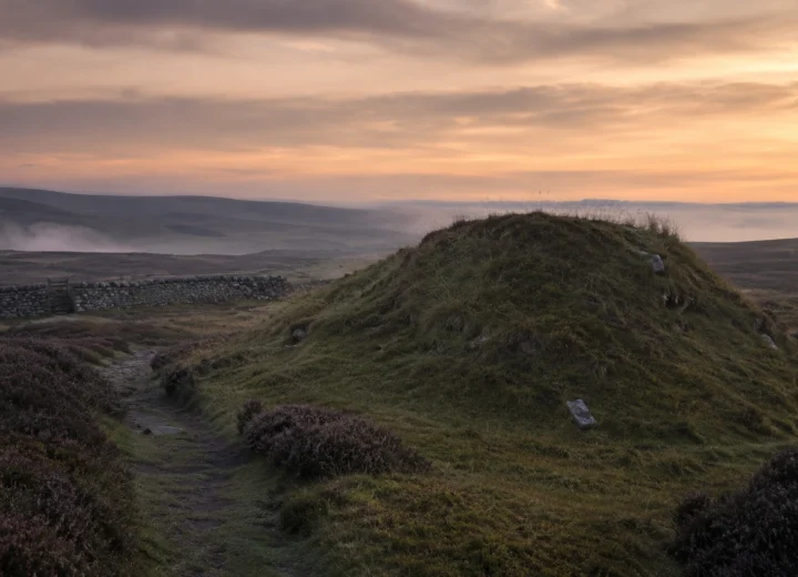 Misty British hillside with an old grassy mound and narrow path associated with the Fair Folk in British folklore.